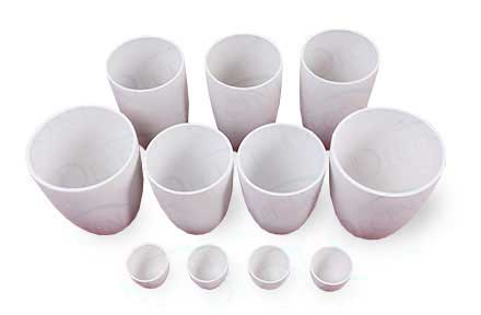 A collection of white, unglazed DECENT crucibles of various sizes, with some mini-crucibles in the foreground, arranged on a white background.