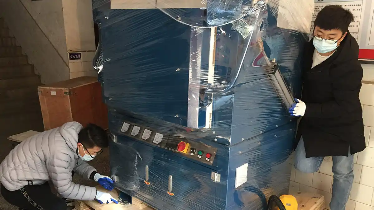 Qingdao Decent Group two engineers, wearing masks and gloves, carefully unloading a fire assay fusion furnace from its packaging, highlighting the delivery and setup process.