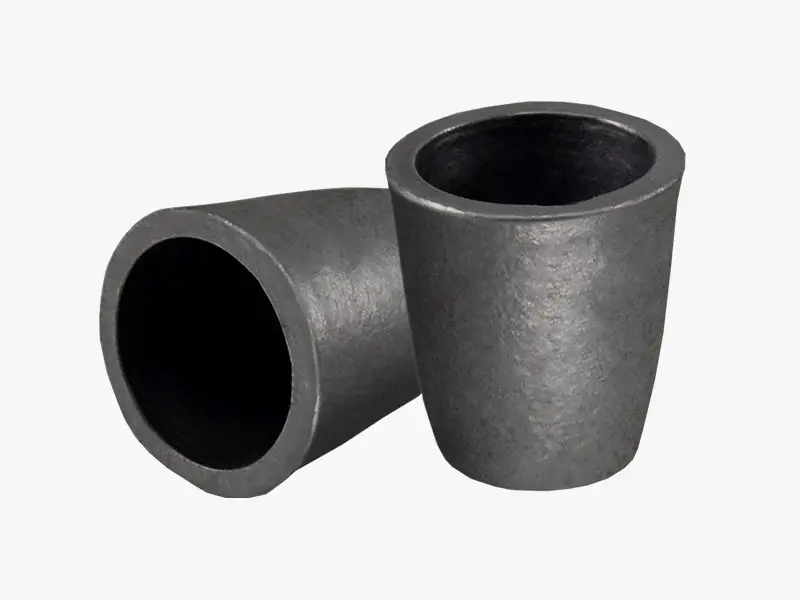 Two dark gray DECENT clay graphite crucibles, one upright and one on its side, showcasing their robust material and conical shape.
