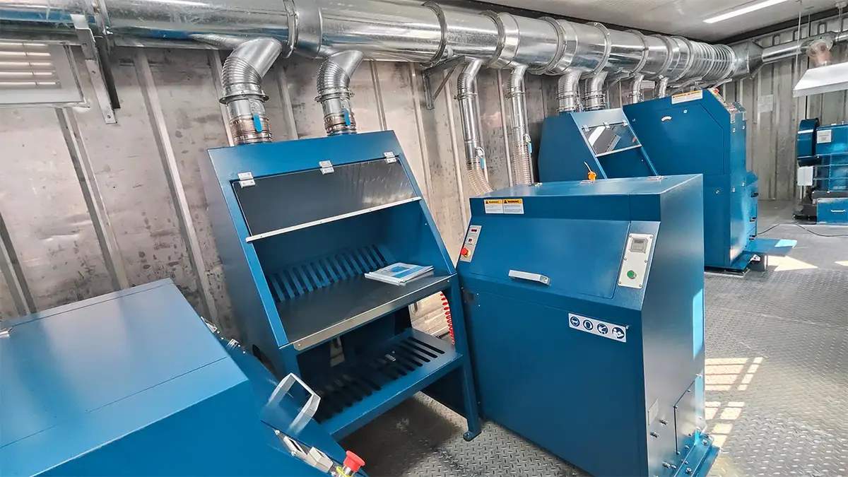 Interior view of the grinding section of a DECENT mobile containerized sample preparation lab, featuring blue industrial crushing and pulverizing equipment with overhead dust extraction systems.