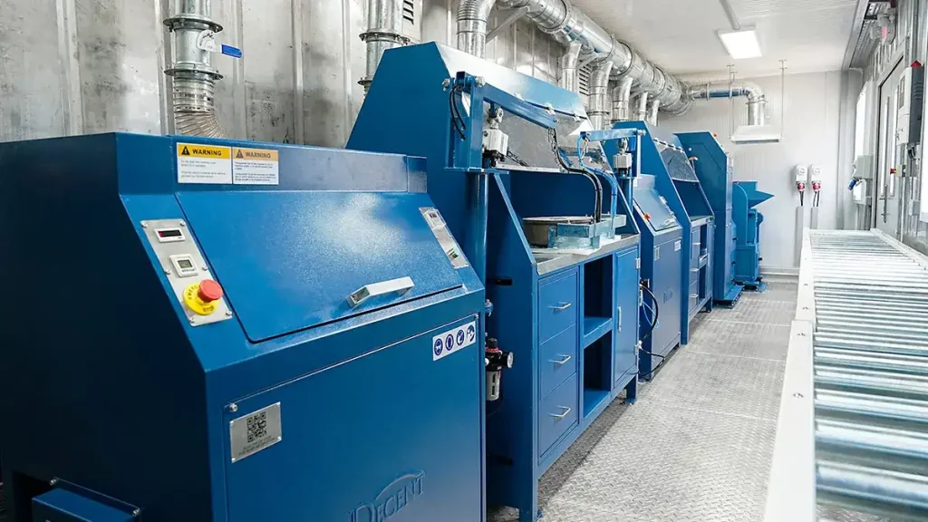 Interior of a DECENT Malaysia Container Laboratory Project 2024 Crushing, Pulverizing, and Dividing Lab, showing a series of blue industrial machines for sample preparation, including a crusher, pulverizer, and sample divider, with overhead ventilation ducts.