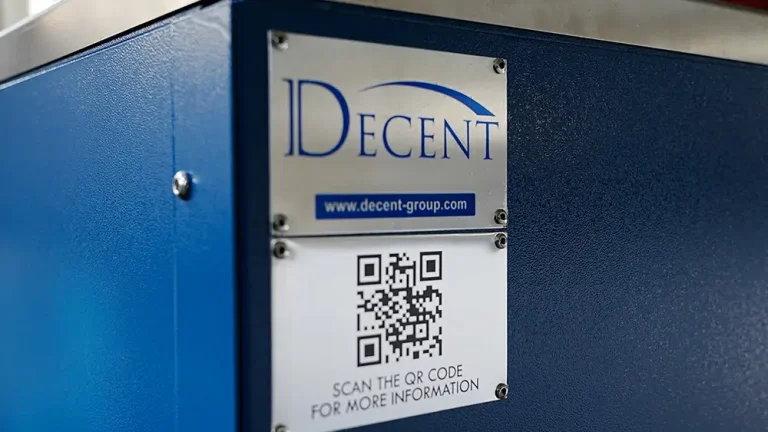 A close-up of a metallic plate with the DECENT logo, company website (www.decent-group.com), and a QR code for more information, affixed to a blue industrial machine