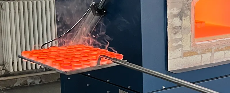 Magnesia cupels glowing red hot on a tray being inserted into a high-temperature fire assay furnace, illustrating DECENT's cupellation process