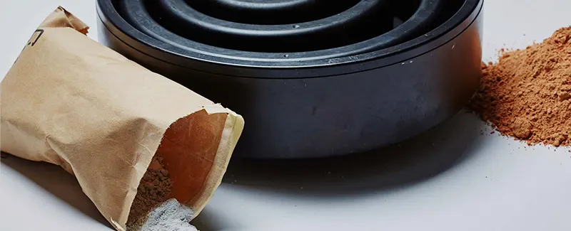 Ground ore powder spilling from a paper bag next to a grinding mill, illustrating DECENT's sample preparation process