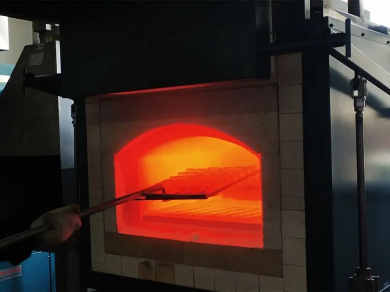 A hand inserting a tray of samples into a glowing hot furnace for precious metal analysis, illustrating DECENT's fire assay process.