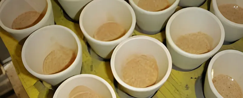 Multiple white crucibles containing powdered mineral samples, prepared for fire assay analysis, representing DECENT's meticulous sample preparation