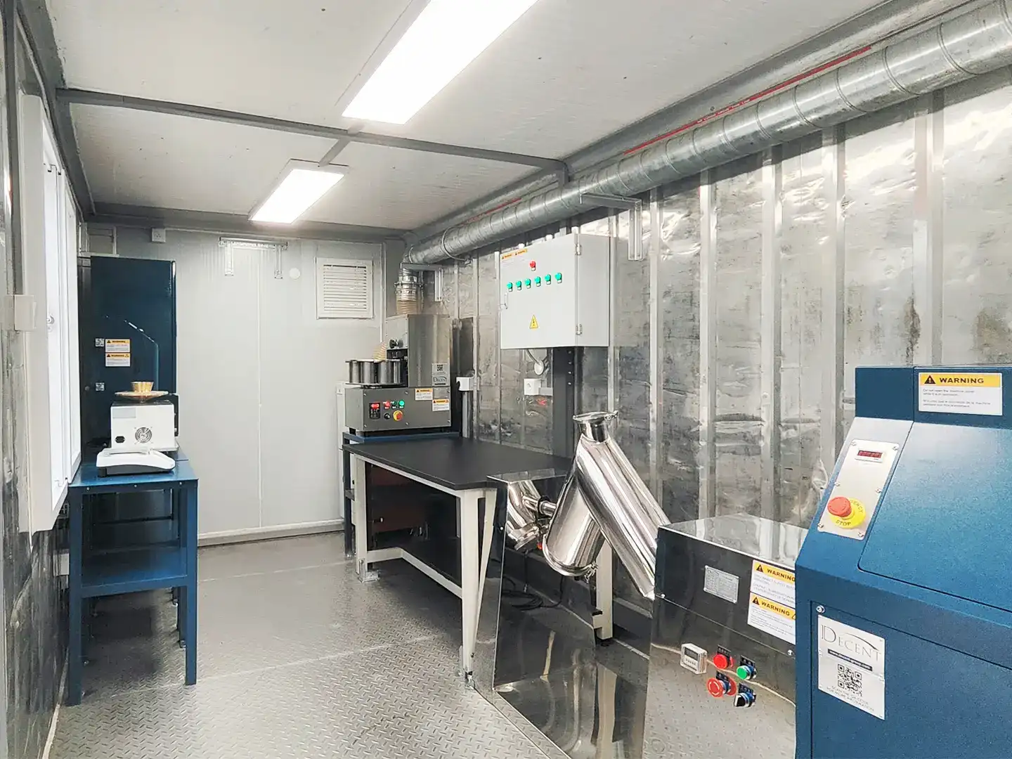 Interior of a fully equipped mobile container laboratory from Qingdao Decent Group, featuring various analytical machines, workbenches, and safety signage.