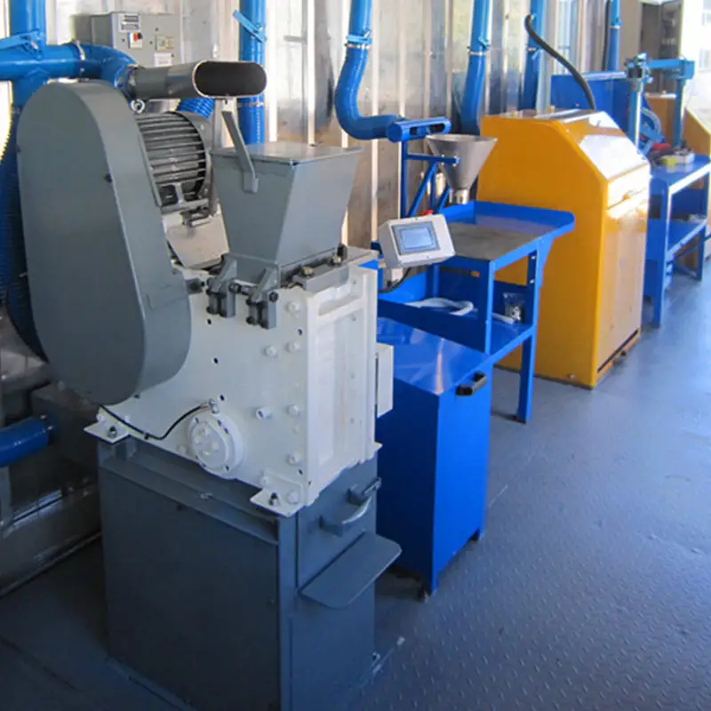 Inside a containerized laboratory, showing a grey jaw crusher and other blue mineral sample preparation machines connected by overhead ventilation ducts.