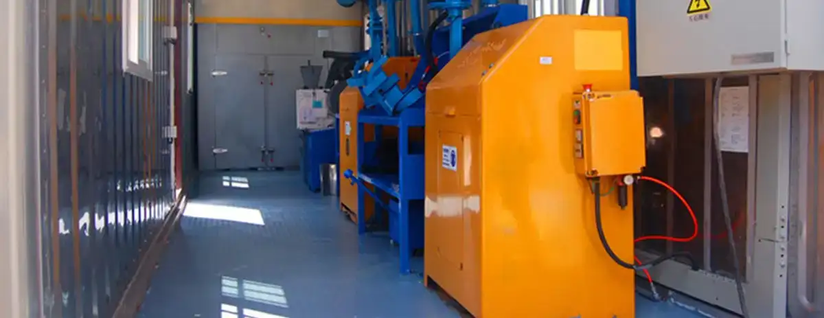 Interior of a mobile containerized laboratory showing mineral sample preparation equipment, a ventilation system, and an electrical control panel.