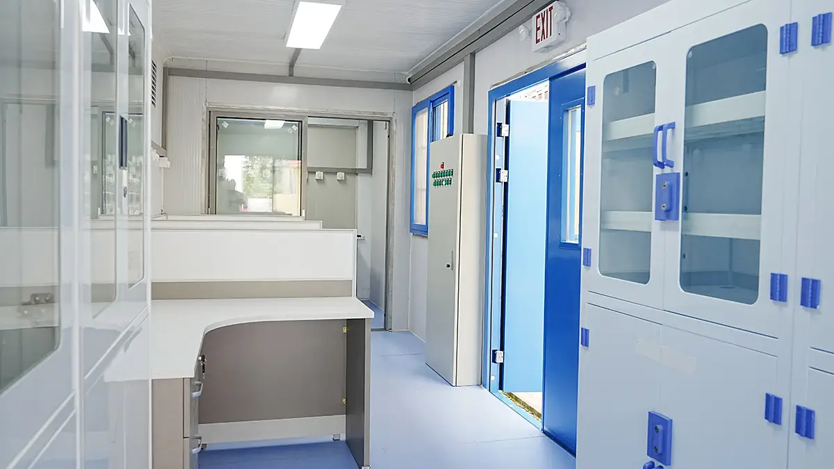 Interior of a DECENT Process-Control XRF Mobile Lab, showing the central office zone with white desks, glass-front cabinets, and a blue door leading to another section.