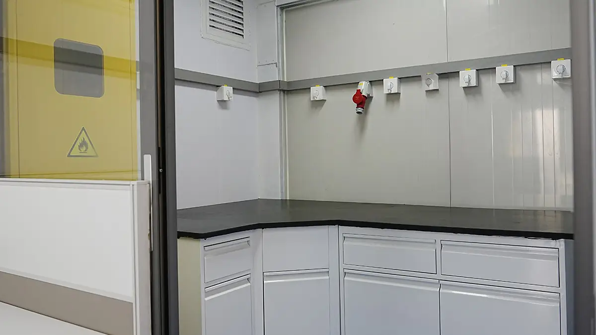 Interior of a DECENT Process-Control XRF Mobile Lab, showing the XRF testing room with lab benches, electrical outlets, and a yellow safety door with a flame warning symbol.