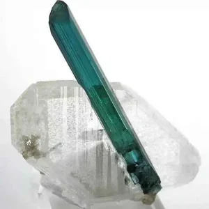 A single, long, prismatic crystal of translucent blue tourmaline, also known as electric stone or indicolite, perched on a clear quartz crystal.