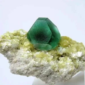 A translucent green fluorite crystal with a dodecahedral shape, resting on a matrix of smaller yellowish-white crystals.