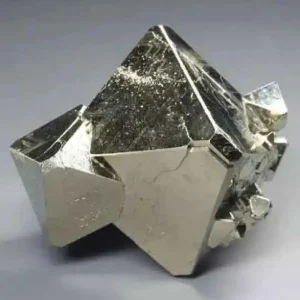 A close-up of a natural platinum crystal, exhibiting a metallic luster and distinct geometric facets, against a neutral background.