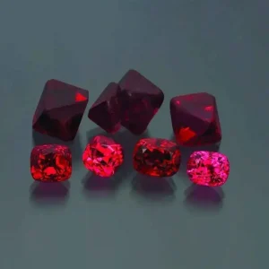A group of brilliant red spinel gemstones, both rough crystals and polished faceted stones, a magnesium aluminum oxide mineral.