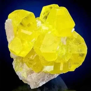 A cluster of bright yellow, translucent sulfur minerals on a light-colored matrix, against a dark blue background.
