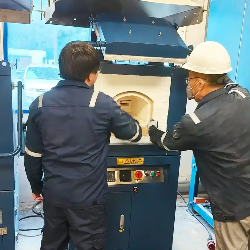 A DECENT team member in safety gear installing and training on a fire assay furnace in a Singapore laboratory.