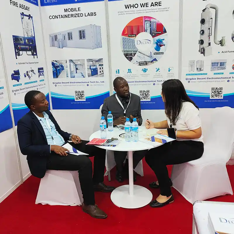 Qingdao Decent Group representative discussing mineral laboratory solutions with two customers at the DECENT booth during Minexpo Tanzania 2025, focusing on customer needs.